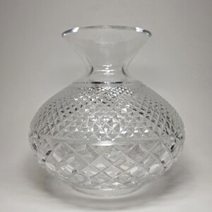 May include: A clear, cut-glass vase with a rounded body and a flared neck. The vase features a diamond-cut pattern across its surface, creating a textured and sparkling appearance. The vase is likely designed for decorative purposes or displaying flowers.