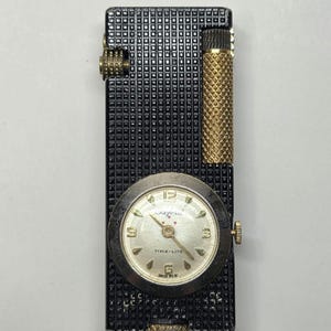 May include: A vintage black lighter with a textured surface and gold accents. It features a round watch with a silver face and the text "TIME-LITE". The watch displays the numbers 12, 3, 6, and 9.