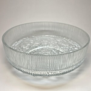 May include: A clear glass bowl with a textured, ribbed exterior and a decorative pattern on the interior base. The bowl has a wide, shallow design, suitable for serving or display. The glass is transparent, allowing light to pass through.