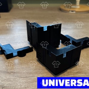 May include: Four black plastic corner brackets, designed for use in woodworking projects. The brackets are L-shaped and have a universal design, making them suitable for a variety of applications. The word "UNIVERSAL" is printed in blue letters on a white background.