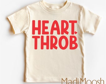 May include: A cream-colored t-shirt with the words "HEART. THROB" in bold red letters. A small red heart is placed after the word "HEART". The brand name "MadiMoosh" is printed in a brown font at the bottom.