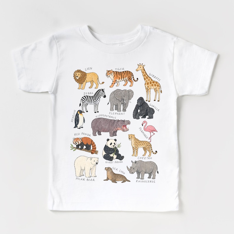May include: White t-shirt featuring a colorful illustration of various animals, including a lion, tiger, giraffe, zebra, elephant, gorilla, and more. Each animal is labeled with its name in a playful font, making it a fun and educational design.