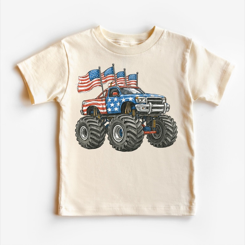 Pode incluir: T-shirt creme com um design de monster truck. O caminh&atilde;o &eacute; decorado com as cores vermelho, branco e azul, e bandeiras americanas. O caminh&atilde;o tem pneus grandes e &eacute; um design patri&oacute;tico.