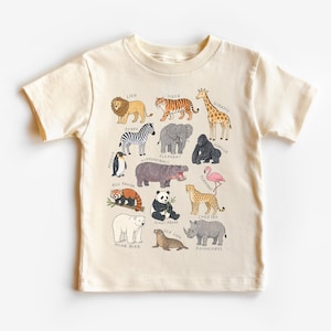 May include: Cream-colored t-shirt featuring a colorful illustration of various zoo animals, including a lion, tiger, giraffe, zebra, elephant, gorilla, and more. Each animal is labeled with its name in a playful font. A fun and educational design.