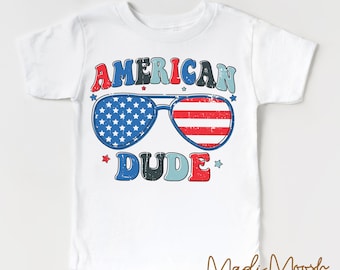 May include: White t-shirt featuring a red, white and blue American flag design. The design includes sunglasses with the American flag pattern and the text "AMERICAN DUDE".