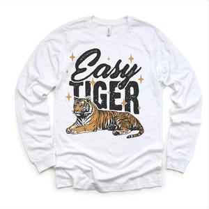 Op de afbeelding: Witte longsleeve t-shirt met een zwarte en gouden afbeelding van een tijger en de tekst "Easy Tiger".