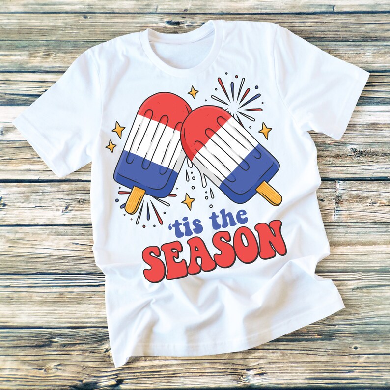 May include: White t-shirt with a red, white, and blue popsicle graphic and the text "'tis the season" in red.