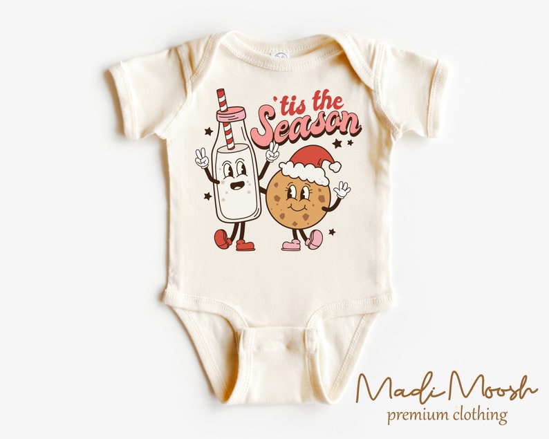 May include: A cream-coloured baby bodysuit featuring a cartoon milk carton and cookie, both smiling and giving peace signs. The text "'tis the season" is above them. The bodysuit is from Madi Moosh premium clothing.