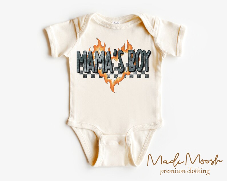 May include: Cream-colored baby onesie with the text "MAMA'S BOY" in a checkered and flame design. The onesie is short-sleeved and has a simple, classic design, perfect for a baby.