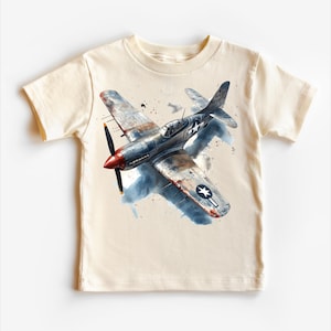 May include: A beige t-shirt with a watercolor illustration of a vintage fighter plane. The plane is painted in blue, gray, and red with a white star on the wing.