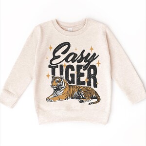 Op de afbeelding: Een beige sweatshirt met een zwarte en gouden grafische print van een tijger en de tekst "Easy Tiger".