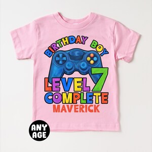 May include: Pink t-shirt with a rainbow colored graphic of a video game controller and the text "Birthday Boy Level 7 Complete Maverick".