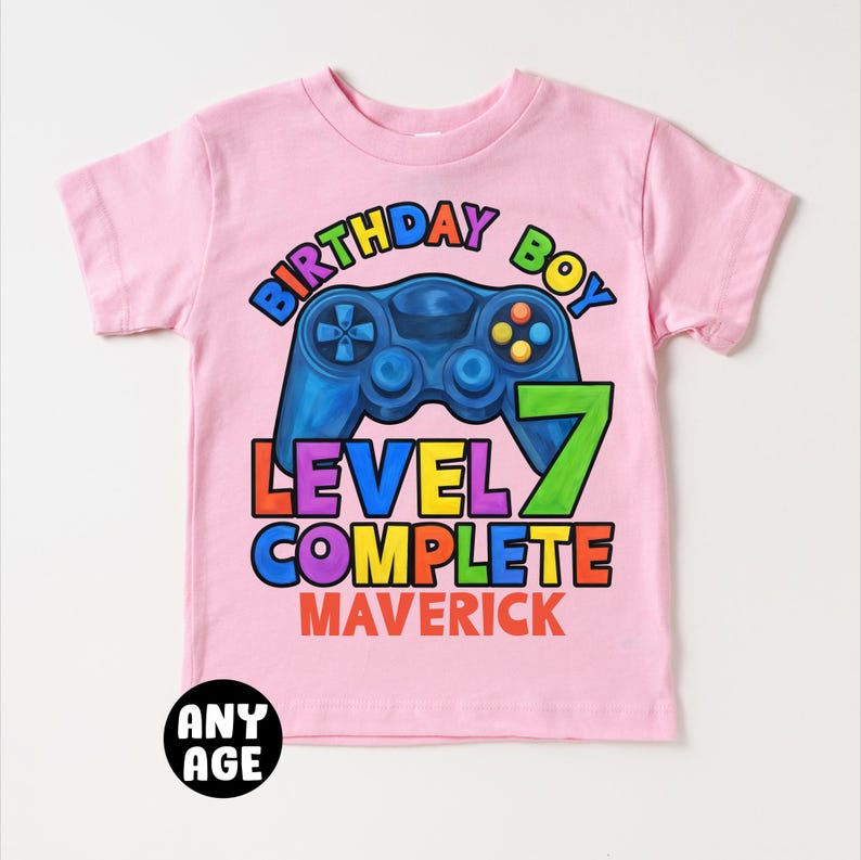 May include: Pink t-shirt with a rainbow colored graphic of a video game controller and the text "Birthday Boy Level 7 Complete Maverick".