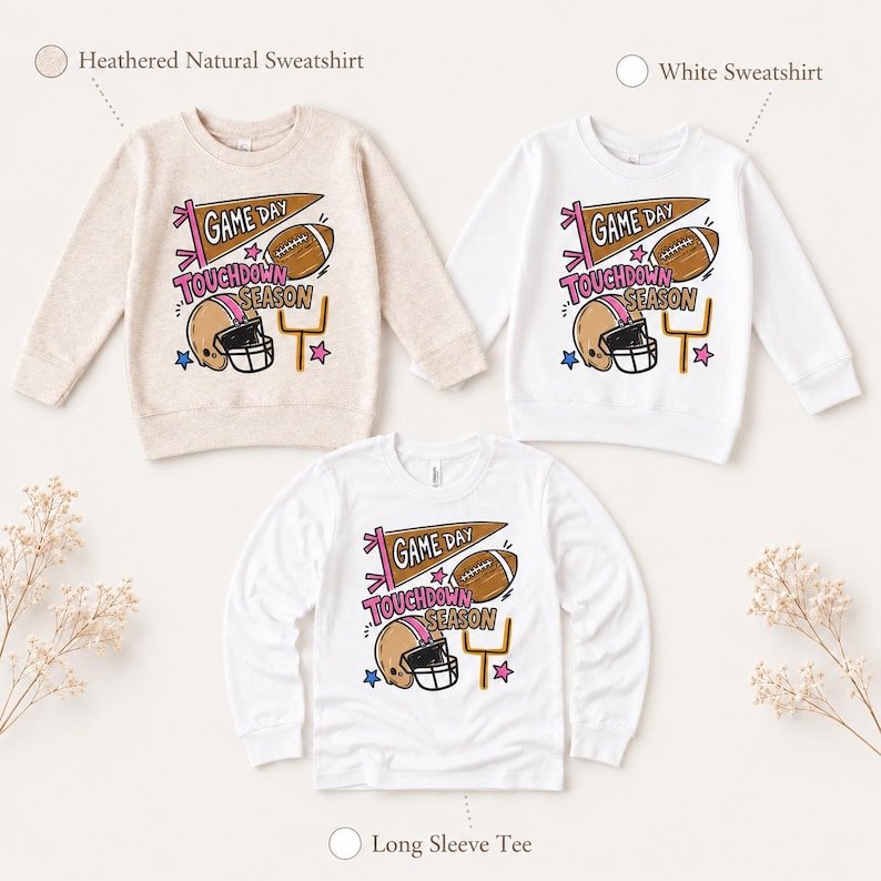 May include: Three long-sleeve shirts in heathered natural and white colors. Each features a graphic with a brown football, a tan helmet, a yellow goal post, and a brown pennant flag with the text GAME DAY and TOUCHDOWN SEASON in pink.