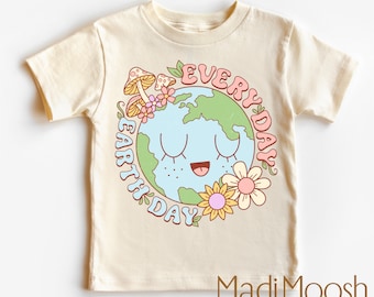 Peut inclure: Un t-shirt crème avec une illustration de la Terre souriante avec des fleurs et des champignons. Le texte "Every Day Earth Day" est écrit en cercle autour de la Terre.