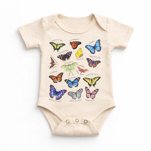 May include: Cream-colored baby onesie featuring a colorful butterfly graphic. The design includes various butterfly illustrations with their names, such as Monarch, Painted Lady, and Swallowtail. The onesie has short sleeves and snap closures.