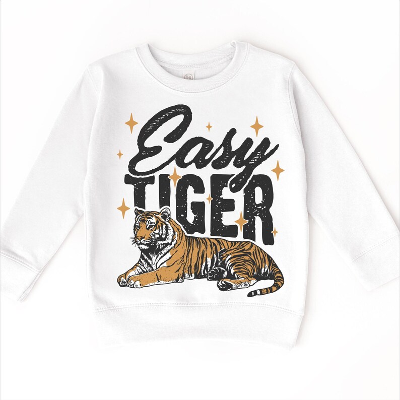 Op de afbeelding: Witte longsleeve trui met de tekst "Easy Tiger" in zwart met gouden sterren. Een cartoon tijger ligt onder de tekst.