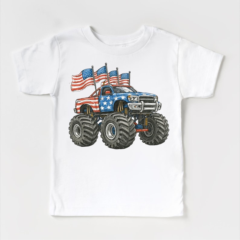 Pode incluir: Camiseta branca com uma ilustra&ccedil;&atilde;o de desenho animado de um monster truck. O caminh&atilde;o &eacute; decorado com a bandeira americana e tem pneus pretos grandes. V&aacute;rias bandeiras tremulando criam um tema patri&oacute;tico.