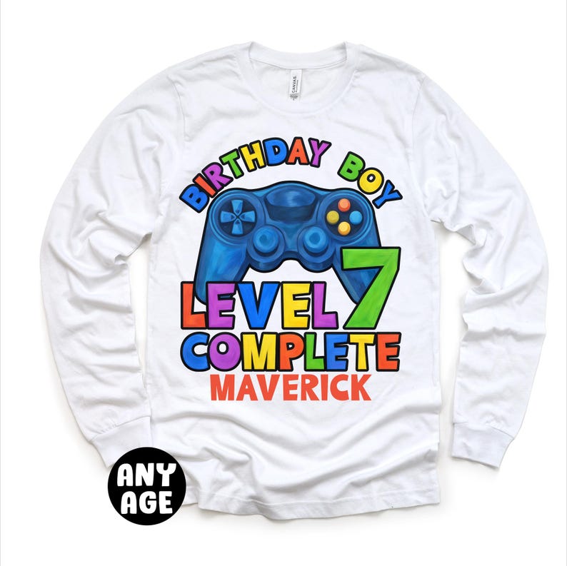 May include: White long-sleeve t-shirt with a colorful graphic of a video game controller and the text "Birthday Boy Level 7 Complete Maverick".
