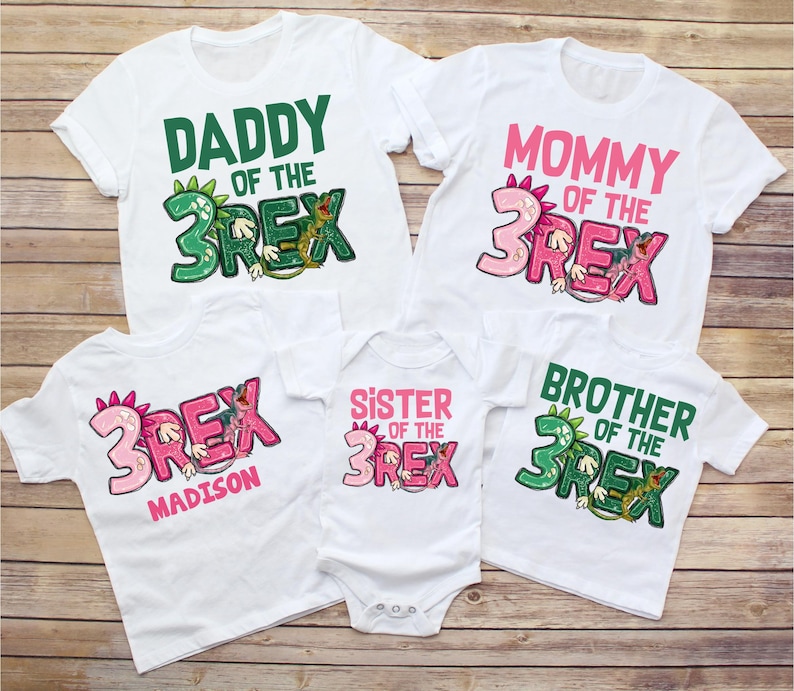 May include: Set of five white t-shirts with green and pink dinosaur graphics. The shirts say "Daddy of the 3Rex", "Mommy of the 3Rex", "Sister of the 3Rex", "Brother of the 3Rex", and "Madison" with a pink dinosaur graphic.