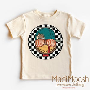 May include: Cream-colored t-shirt featuring a cartoon turkey wearing sunglasses that read "GOBBLE GOBBLE" inside a black and white checkered circle. The turkey is wearing a teal baseball cap and a red bow tie. The shirt has the text "MadiMoosh premium clothing" at the bottom.