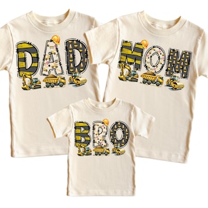 May include: Three cream colored t-shirts with a construction theme. The shirts say "DAD", "MOM", and "BRO" with construction vehicles and yellow and black stripes.