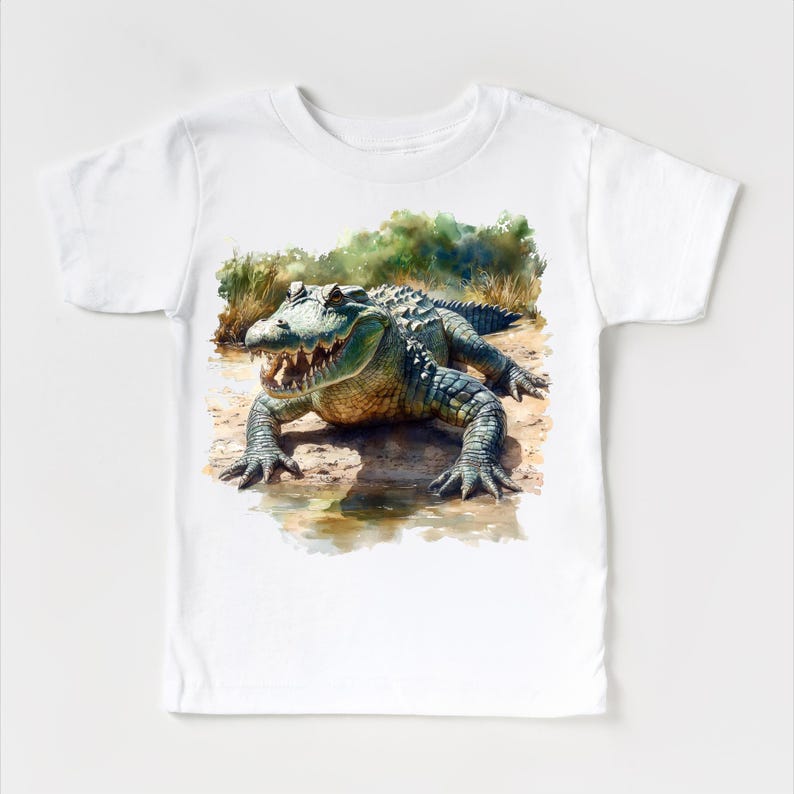 K&ouml;nnte beinhalten: Wei&szlig;es T-Shirt mit einer Aquarell-Illustration eines Alligators mit offenem Maul vor einem gr&uuml;n-braunen Hintergrund.