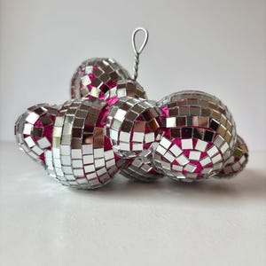May include: A cluster of silver disco balls with pink centers, connected by a silver wire.