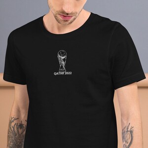 May include: Black t-shirt with a white graphic of the FIFA World Cup trophy and the text "QATAR 2022".