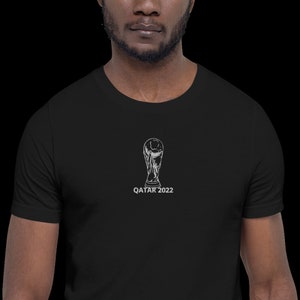 May include: A black t-shirt with a white graphic of the FIFA World Cup trophy and the text "QATAR 2022".