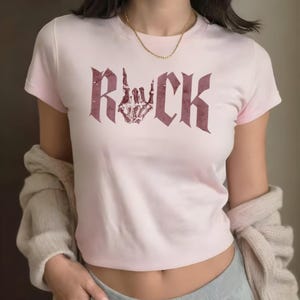 A woman wearing a pink t-shirt with the word "ROCK" printed on it, along with a skeleton hand graphic.