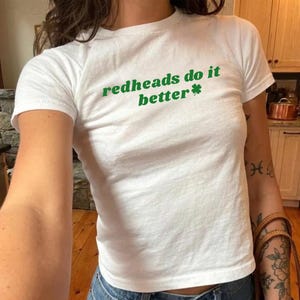 May include: White t-shirt with the text "redheads do it better" in green, along with a green shamrock. The shirt has short sleeves and a crew neck. The shirt is made of a soft, comfortable material.