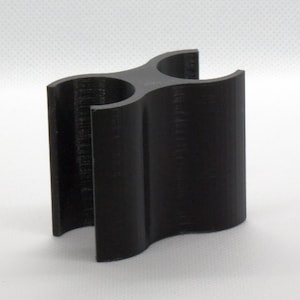 May include: A black, 3D-printed object with a unique, three-section design. The object has a curved shape and is made of a solid, dark material. The overall form is reminiscent of a stylized holder or stand.