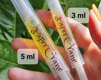 May include: Two clear plastic bottles with white applicators and yellow liquid. The bottles are labeled "Paper Crane" and have the text "3 ml" and "5 ml" printed on them.