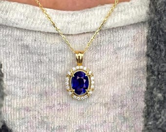 May include: A gold chain necklace featuring an oval-shaped blue sapphire pendant surrounded by a halo of small white diamonds. The pendant is set in a gold frame with prongs, suspended from a delicate gold link chain resting against the neck.