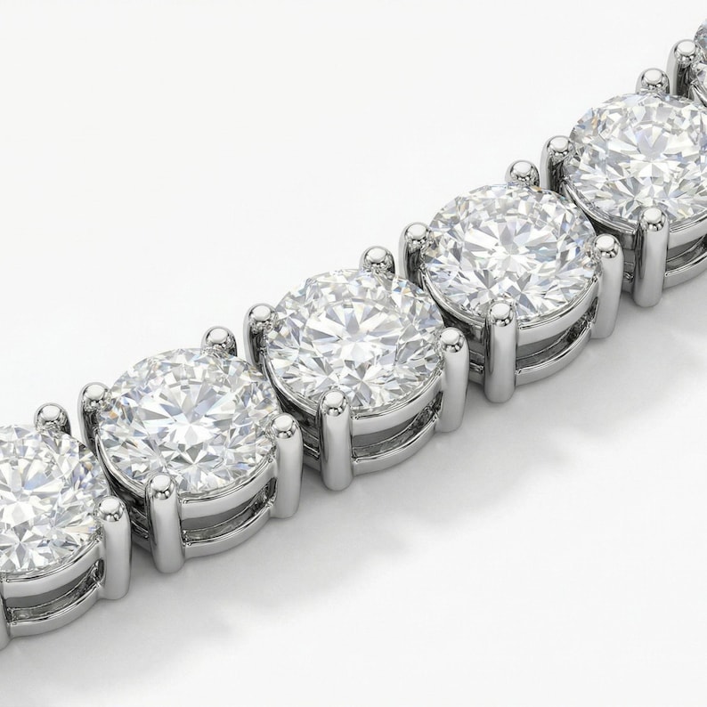 May include: Close-up of a diamond tennis bracelet. The bracelet features a series of large, round-cut diamonds set in a silver or platinum metal. The diamonds are clear and sparkling, reflecting light. The setting is a classic prong style.