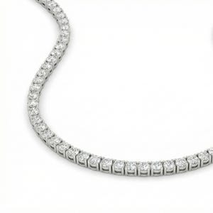 May include: A sparkling, silver-toned tennis necklace. The necklace is composed of numerous round, clear gemstones set closely together. The gemstones are evenly spaced and create a continuous line of brilliance. The background is a clean, bright white.