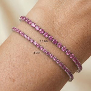 May include: Two pink gemstone bracelets, 2 mm and 2.5 mm, are displayed on a wrist. The bracelets are made of small, round, pink gemstones set closely together. The gemstones are a vibrant pink color, and the bracelets appear to be made of silver or a similar metal.
