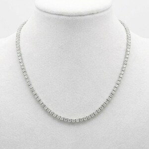 May include: A tennis necklace with a continuous line of round-cut, clear gemstones. The necklace is displayed on a white mannequin bust, showcasing its delicate design and sparkle. The gemstones are evenly spaced, creating a classic and elegant look.