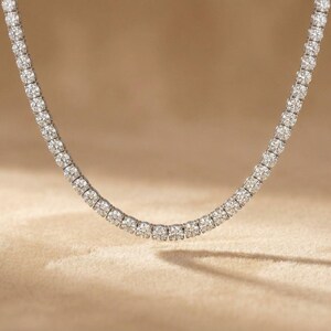 May include: A sparkling necklace featuring a continuous line of round-cut diamonds. The diamonds are set closely together, creating a brilliant display of light. The necklace is displayed against a neutral background, highlighting its elegance.