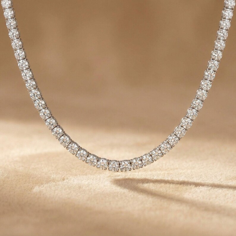 May include: A sparkling necklace featuring a continuous line of round-cut diamonds. The diamonds are set closely together, creating a brilliant display of light. The necklace is displayed against a neutral background, highlighting its elegance.