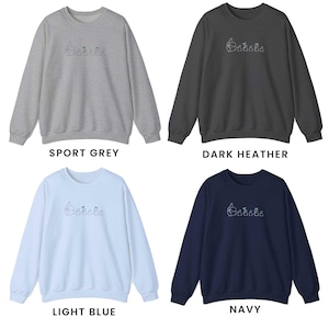 K&ouml;nnte beinhalten: Vier Rundhals-Sweatshirts in verschiedenen Farben: Sportgrau, Dunkelgrau meliert, Hellblau und Marineblau. Jedes Sweatshirt hat ein kleines gesticktes Design einer Gruppe von Pinguinen mit H&uuml;ten.