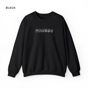 Puede incluir: Sudadera negra con un contorno blanco de personajes de dibujos animados en la parte delantera. Los personajes incluyen Totoro, Sin Cara, Jiji, Kiki y una calavera.