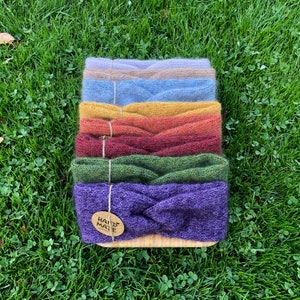 Può includere: Un set di sei fasce per capelli in maglia colorate in tonalità viola, verde, rosso, giallo, blu e beige. Le fasce sono disposte a forma di arcobaleno e hanno un'etichetta