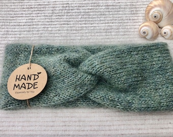 Op de afbeelding: Een groene gebreide hoofdband met een bruin label waarop "HAND MADE Especially for You" staat.