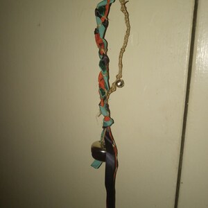 Puede incluir: Un cordón trenzado con una cinta negra, tela naranja y turquesa, y cascabeles plateados colgando de una puerta.