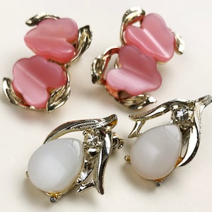 May include: Two pairs of vintage earrings. One pair features pink, flower-shaped stones set in gold-tone metal. The other pair has white, teardrop-shaped stones with a small clear gem and gold-tone metal.