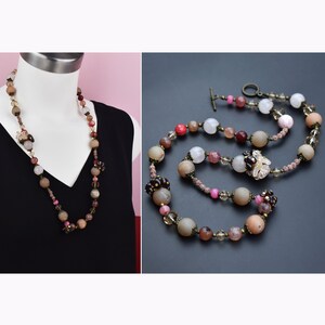 Puede incluir: Un collar largo con una mezcla de cuentas beige, rosa, marrón y transparentes. El collar tiene cuentas grandes y redondas y otras más pequeñas y facetadas, con adornos florales. Se muestra sobre un maniquí y sobre un fondo oscuro. Aproximadamente 70 cm de largo.