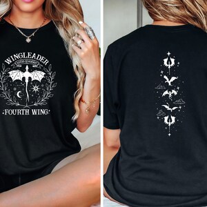 May include: Black t-shirt with a white graphic of a dragon and the text "WINGLEADER FOURTH WING". The back of the shirt has a vertical design of four dragons with stars and clouds.