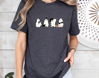 Puede incluir: Una camiseta de manga corta en color gris marengo jaspeado con un estampado gráfico de cuatro fantasmas blancos que interactúan con gatos negros y una pequeña calabaza naranja. Los fantasmas aparecen en varias poses, algunos sosteniendo gatos.